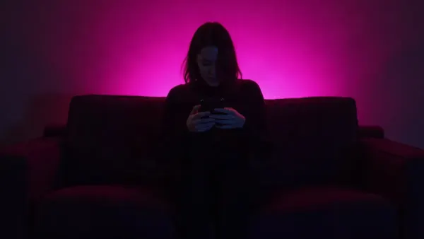 Silhouette de dos sur un canapé tenant un téléphone, dans une pièce sombre à lueur magenta, illustration de l’article « IA sans censure 2026 : les chats IA qui autorisent le NSFW »